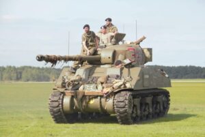 WOII-militairen in uniformen op camouflage tank met kanon in open veld, tank nummer 34, bomen op achtergrond, evenement re-enactment - Agenda World of Veterans