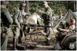 Groep WOII re-enactment in militaire uniformen bij een machinegeweer, met munitieriemen en apparatuur, in een gecamoufleerd kamp, agenda World of Veterans